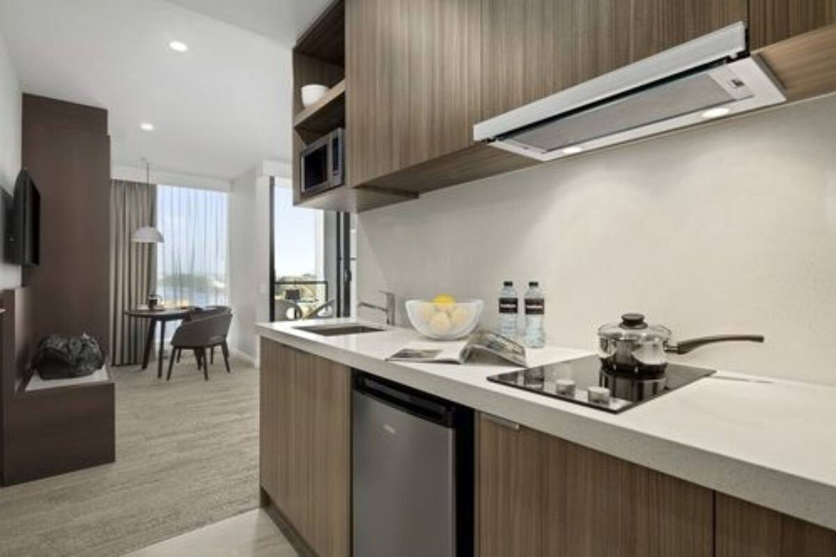 A modern kitchen with a built-in microwave, a coffee maker, and a sink. There is a dining area with a table and chairs visible in the background.