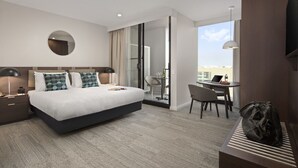 A modern hotel room with a large bed, a desk, and a view of the city. - Quest Innaloo (Innaloo)