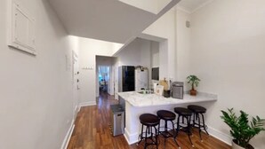 A modern kitchen with a marble countertop, a built-in oven, and a small refrigerator. There are three bar stools and a potted plant on the counter. - Central Park, Theater District & Columbus Circle. New Renovation 3 Bed / 2 Bath. (New York City)