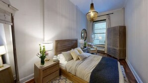 A bedroom with a bed, bedside tables, a nightstand, a dresser, a mirror, a window, and a wardrobe. - Central Park, Theater District & Columbus Circle. New Renovation 3 Bed / 2 Bath. (New York City)