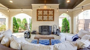 Un patio techado con chimenea de ladrillo, mobiliario exterior e iluminación colgante.