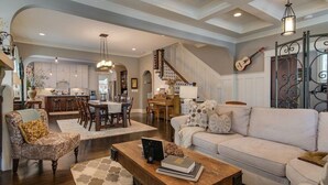 Un salón espacioso con sofá, sillón y mesa de centro. Una escalera conduce a un comedor con una cocina al fondo.