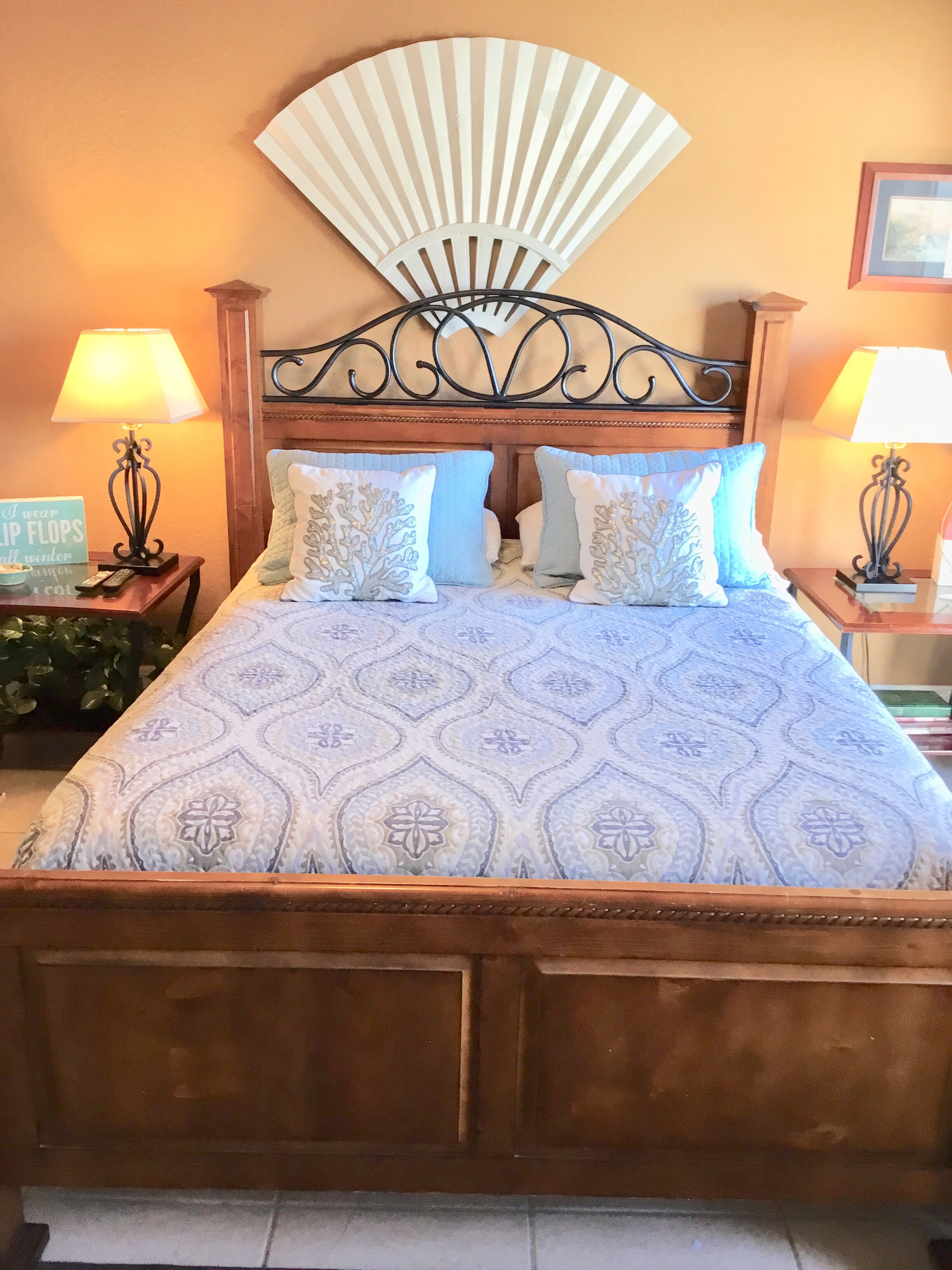 A bed with a patterned bedspread, a decorative fan, and two bedside lamps.