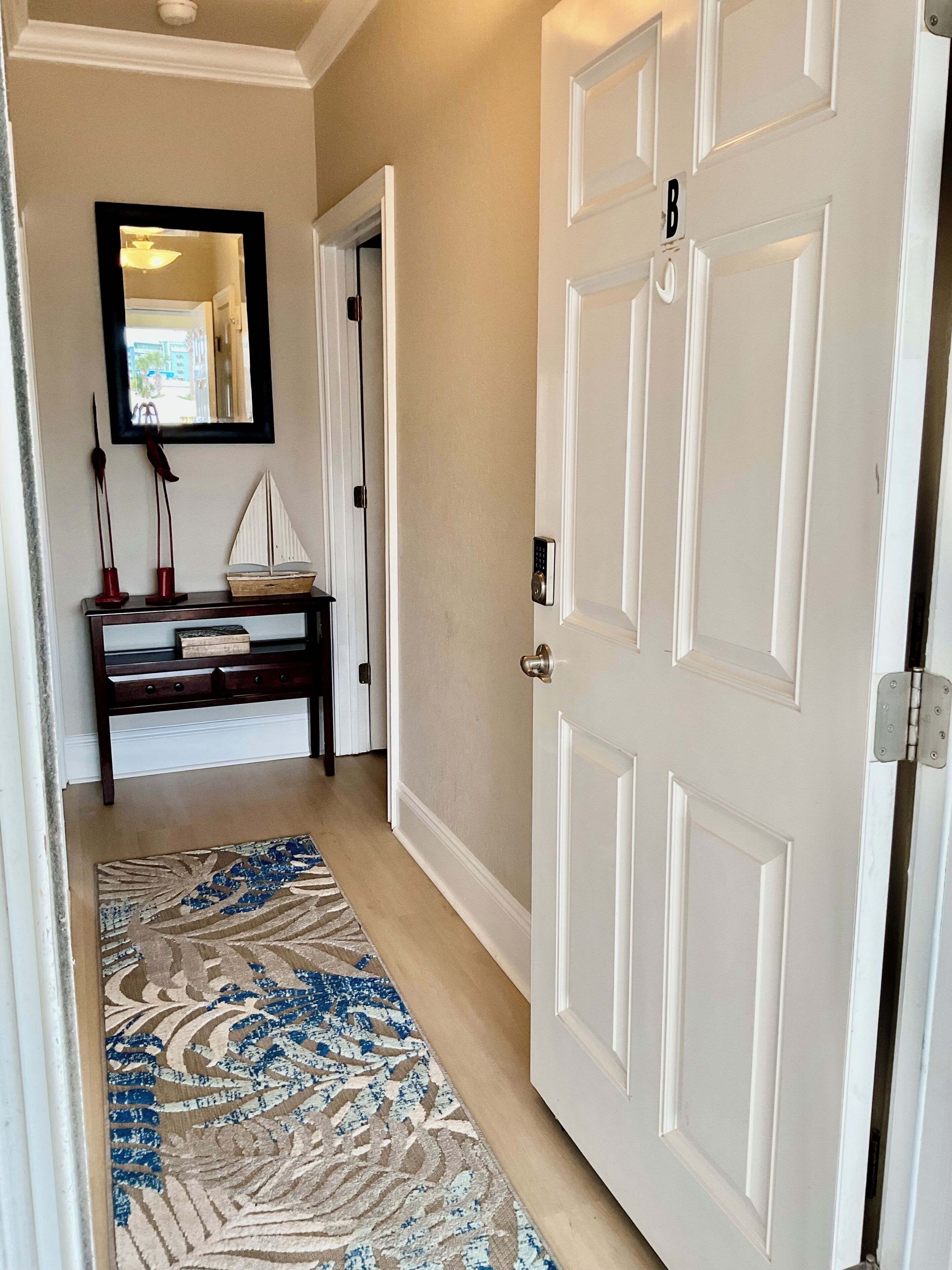 A hallway with a patterned rug, a wooden bench, a mirror, and a white door.