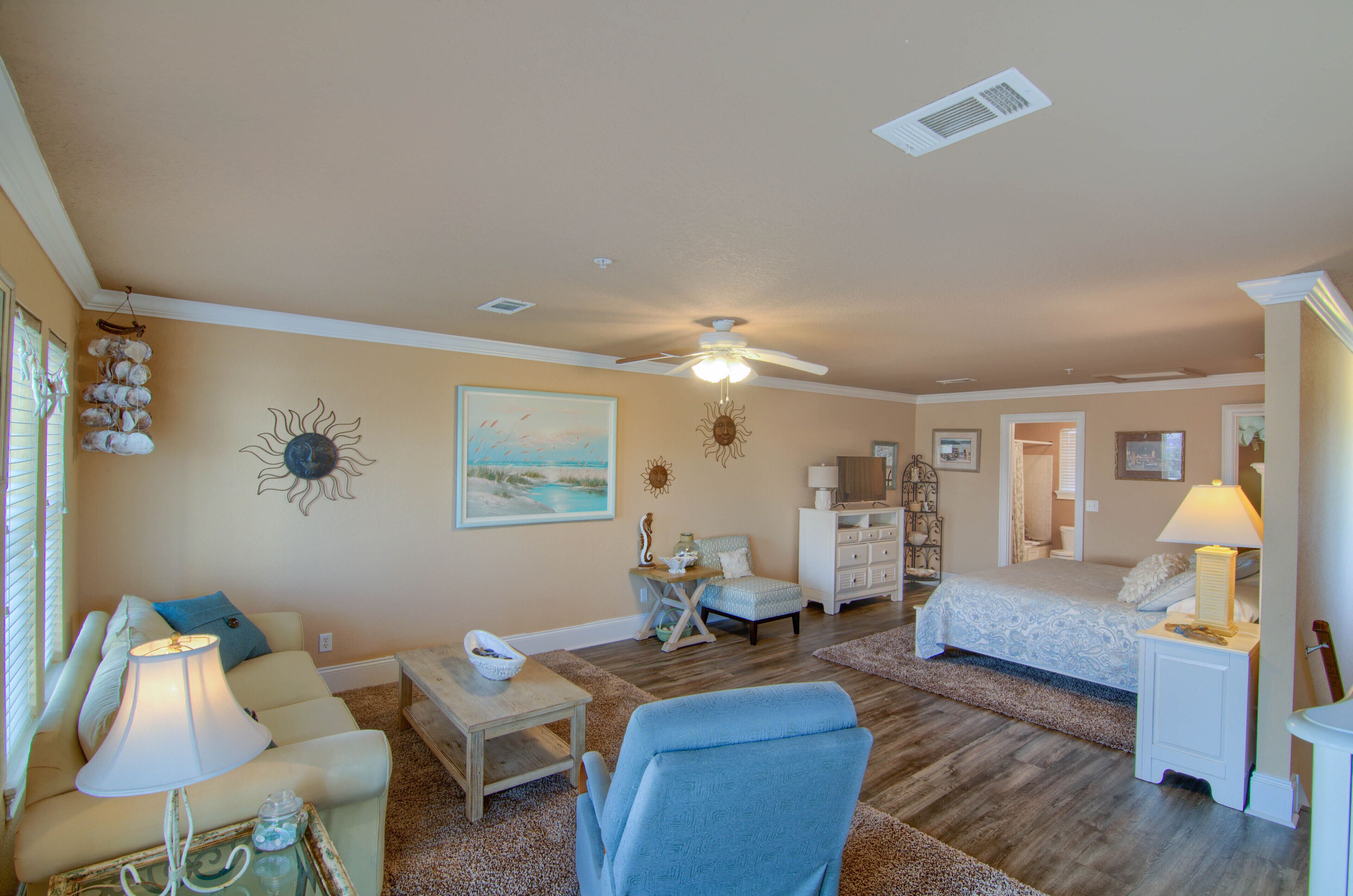 A spacious living room with a ceiling fan, a large painting, and a cozy seating area with a lamp.