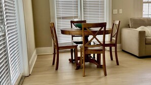 Uma área de refeições com mesa e cadeiras, uma janela com persianas e uma placa acima da janela.