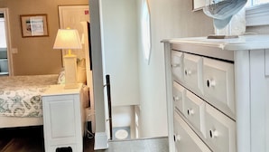 Quarto com cama, mesa de cabeceira, cômoda e decoração de um veleiro pendurado.
