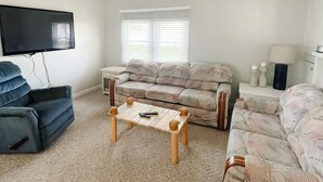 A living room with a flat-screen TV, two sofas, a coffee table, and a window with blinds. - Lake McConaughy Cabin within walking distance to beach!  (Lewellen)