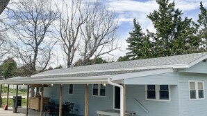 A covered patio area with a table and chairs, a bench, and a grill. - Lake McConaughy Cabin within walking distance to beach!  (Lewellen)