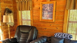 Ein Holzblockhaus-Interieur mit einem Ledersofa, einem Ohrensessel, einem gerahmten Bild und einem Bärenfell.