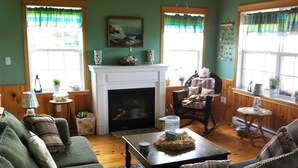 A cozy living room with a fireplace, green walls, wooden floors, and a comfortable seating area. - Gorgeous Oceanfront Vacation Destination! (Saint Peters Bay)