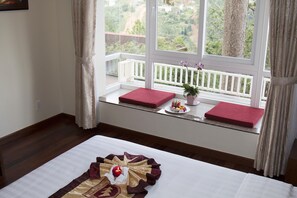 Une chambre d’hôtel avec un lit, une fenêtre donnant sur un balcon et une petite table sur laquelle est disposée une assiette de fruits.