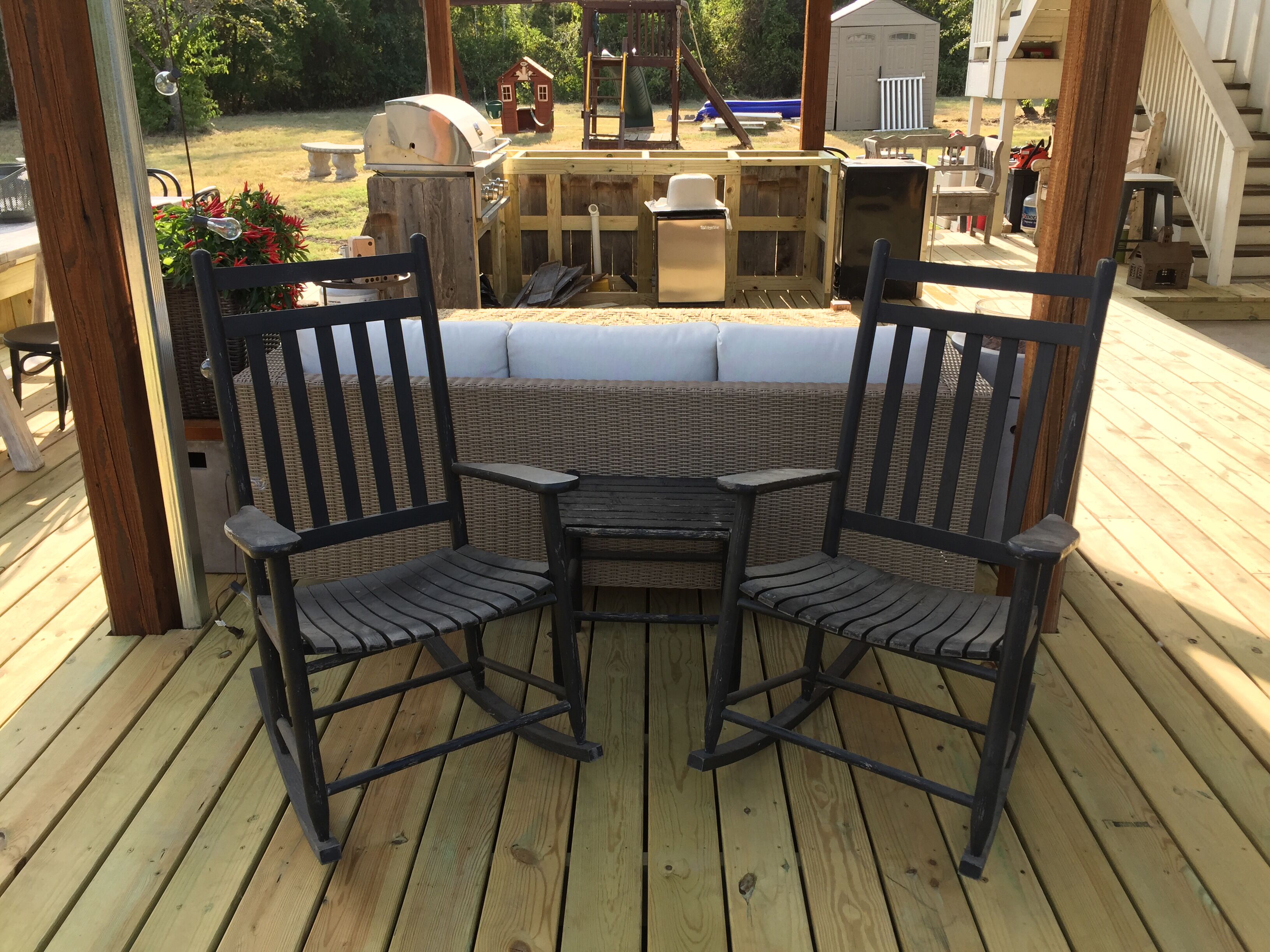 A wooden deck with two black rocking chairs and a small table.
