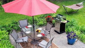 Eine Terrasse mit Glastisch, Stühlen, Grill und Hängematte.