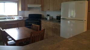 A kitchen with wooden cabinets, a stove, a refrigerator, a dining table with chairs, and a window with natural light. -  A Centrally-Located Vacation Home For All Your Kenai Peninsula Adventures! (Kasilof)