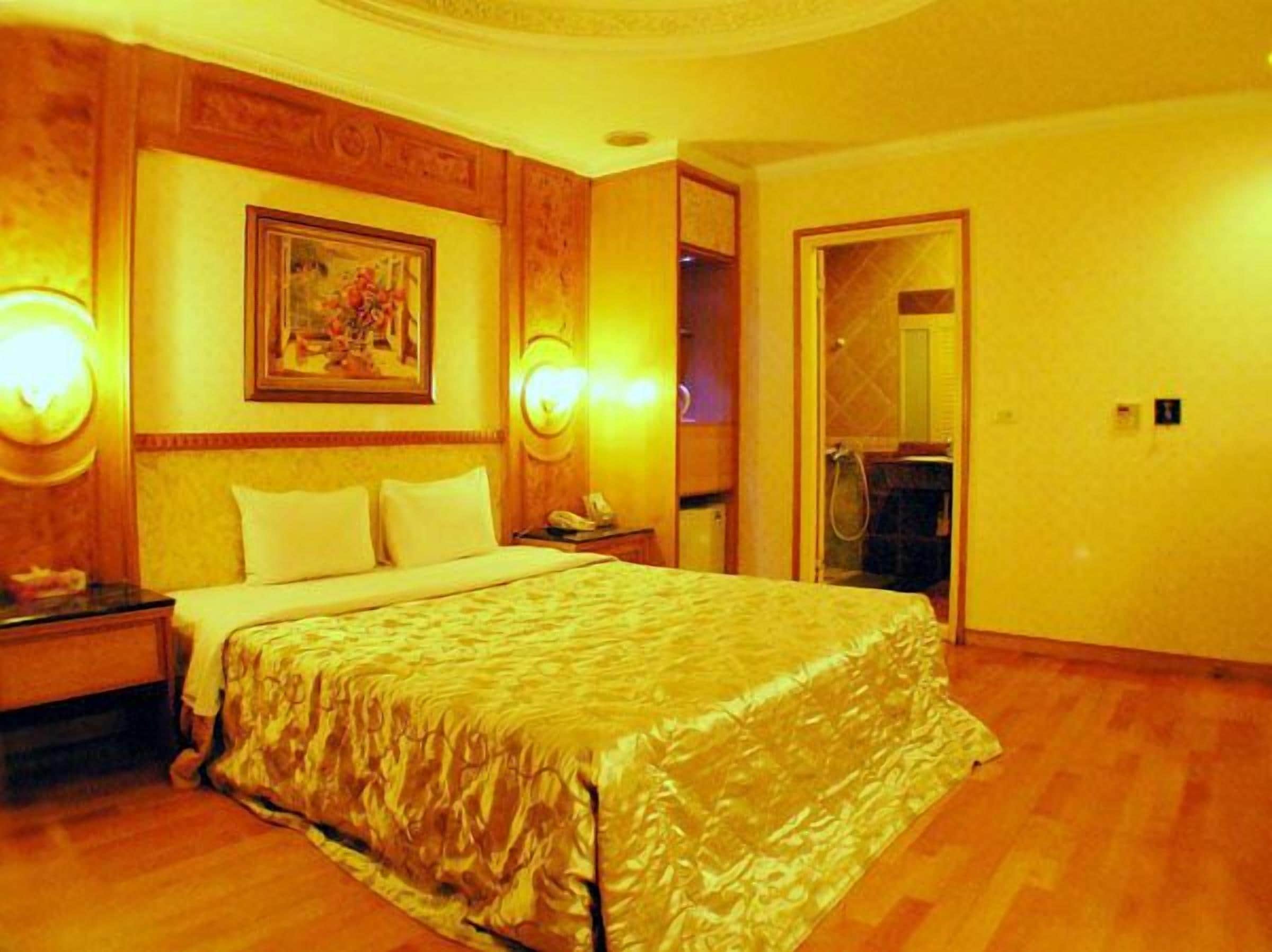 Una camera d'albergo con un letto grande, pannelli in legno, un quadro appeso e un bagno visibile attraverso una porta aperta.