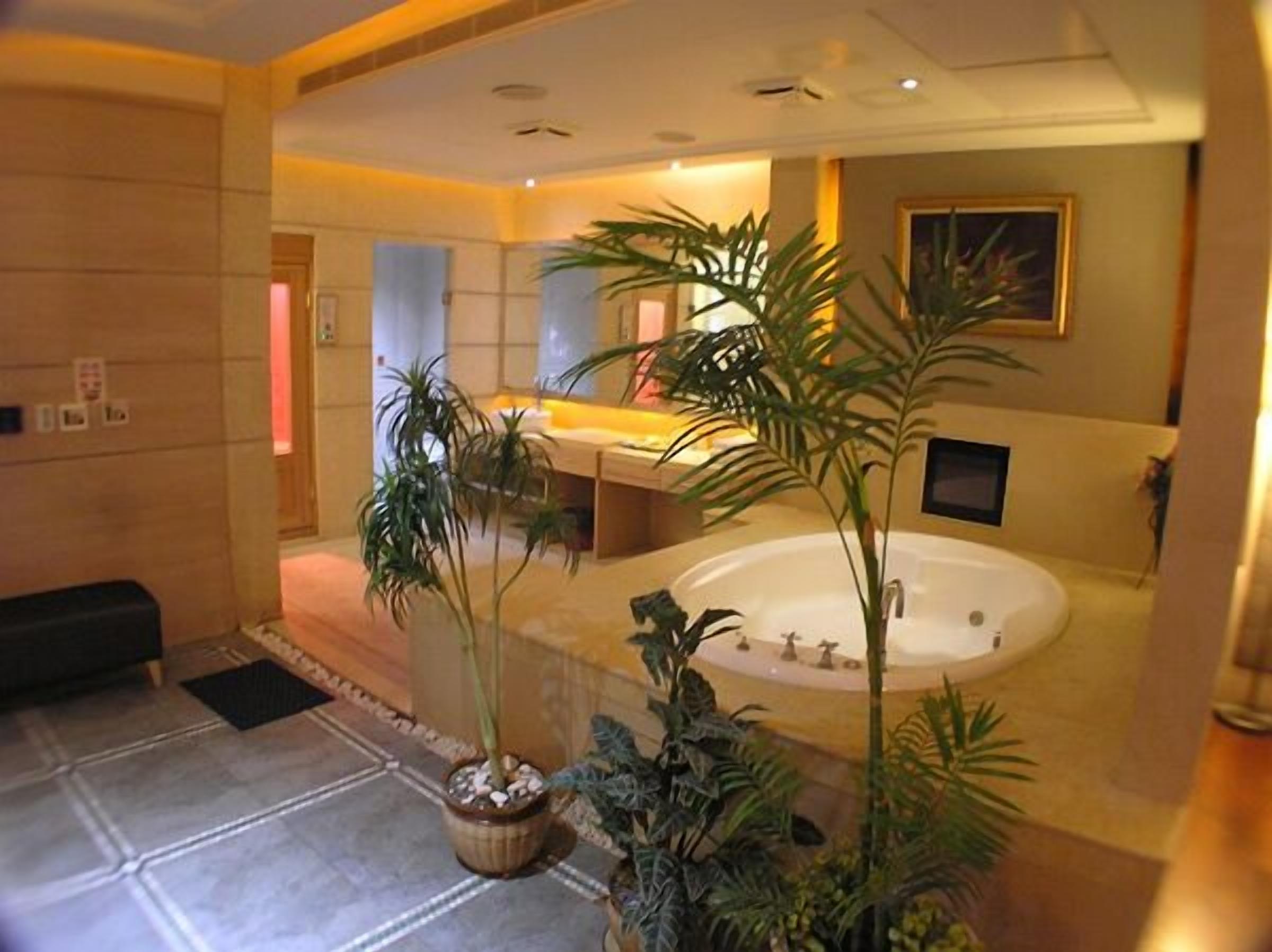 Un baño moderno con una bañera grande, varios lavamanos y varias macetas con plantas.