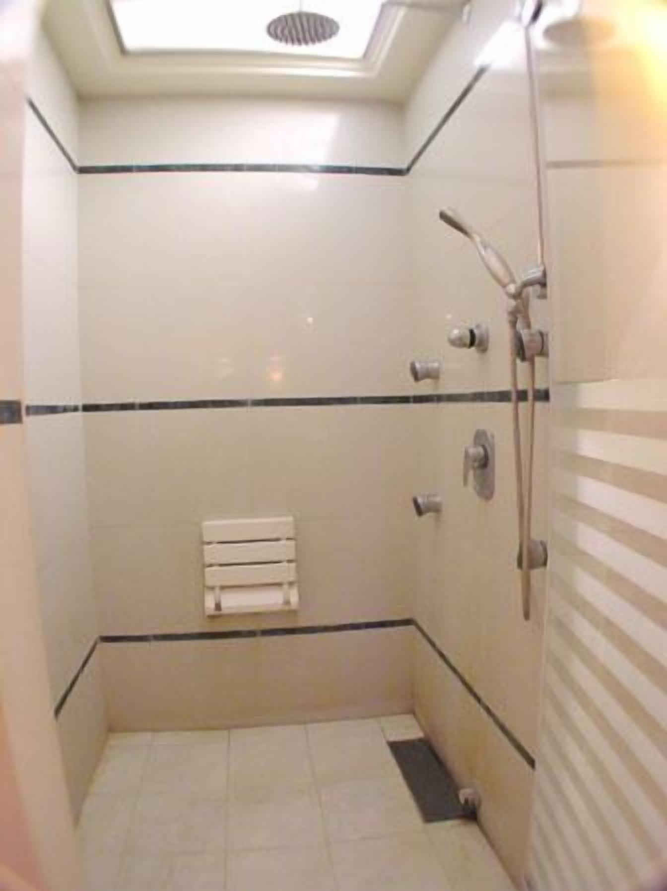 Un baño pequeño con azulejos, un tragaluz, un perchero y un cabezal de ducha.
