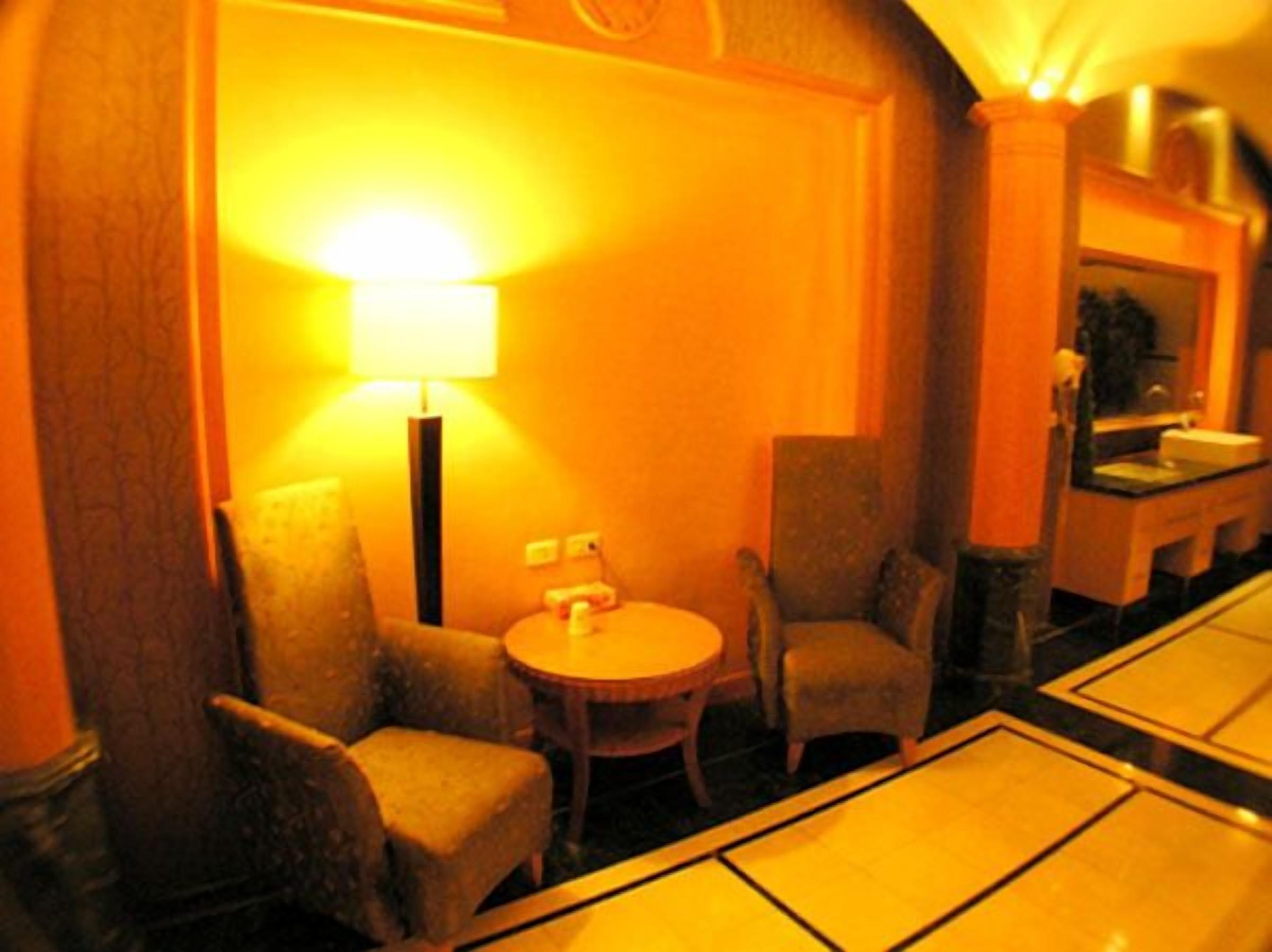 Una habitación de hotel con una mesa redonda, dos sillones, una lámpara y un espejo.