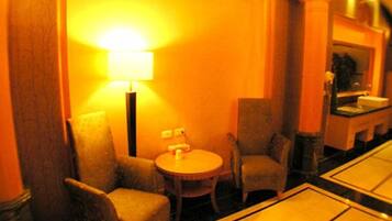 Una habitación de hotel con una mesa redonda, dos sillones, una lámpara y un espejo.