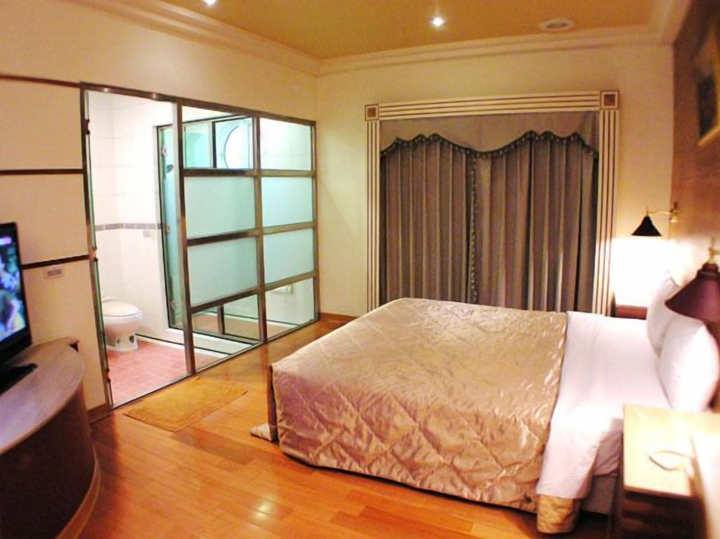 Quarto de hotel com uma cama grande, televisão, escrivaninha e porta de correr para um banheiro.