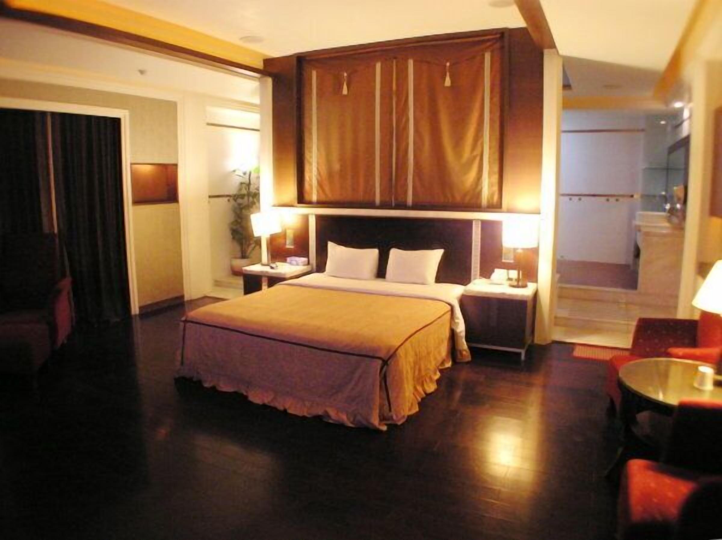 A hotel room with a large bed, two bedside tables with lamps, a wooden headboard, and a view of the hallway.