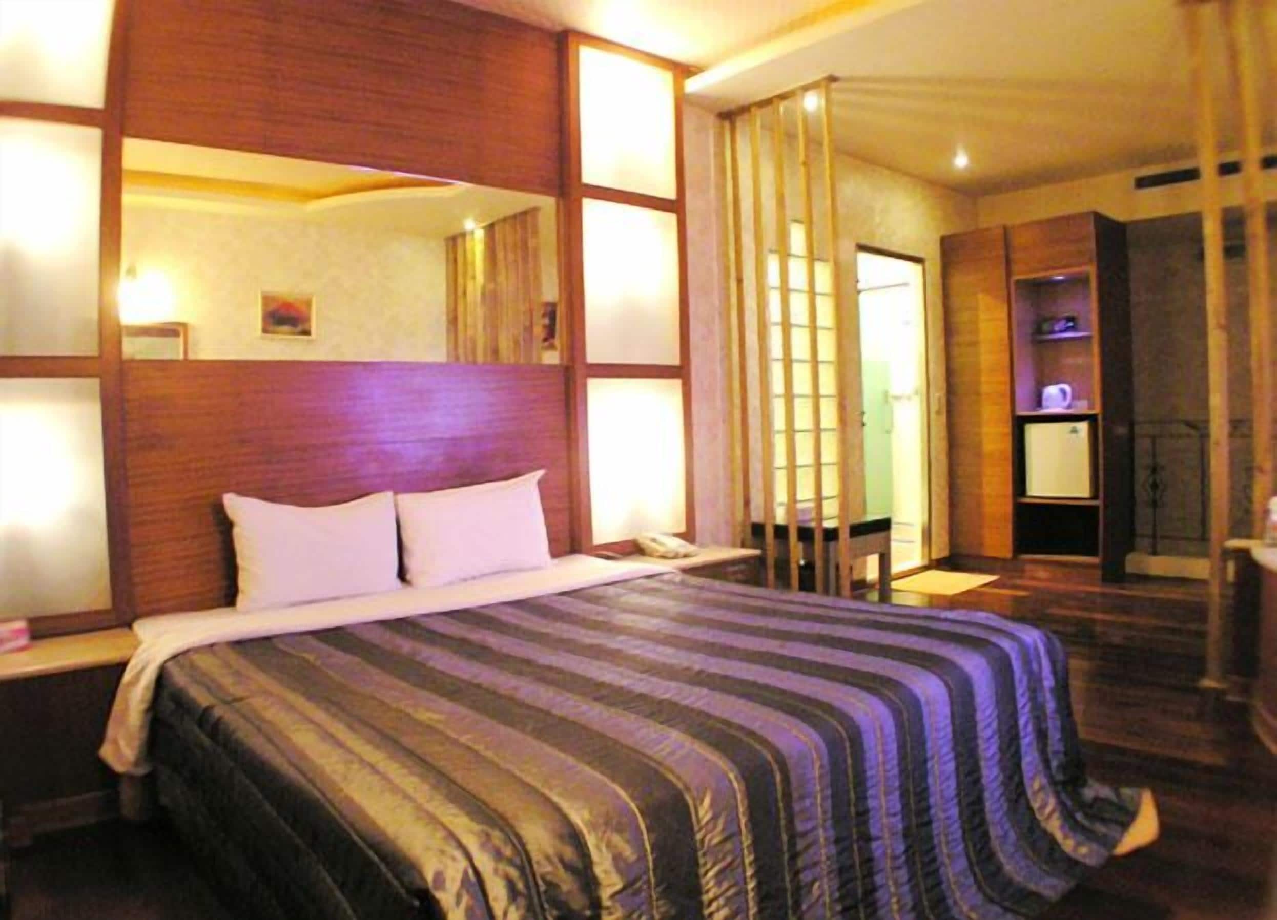 Una habitación de hotel con una cama grande, cabecera de madera y un espejo. Hay un escritorio con una silla y un televisor.