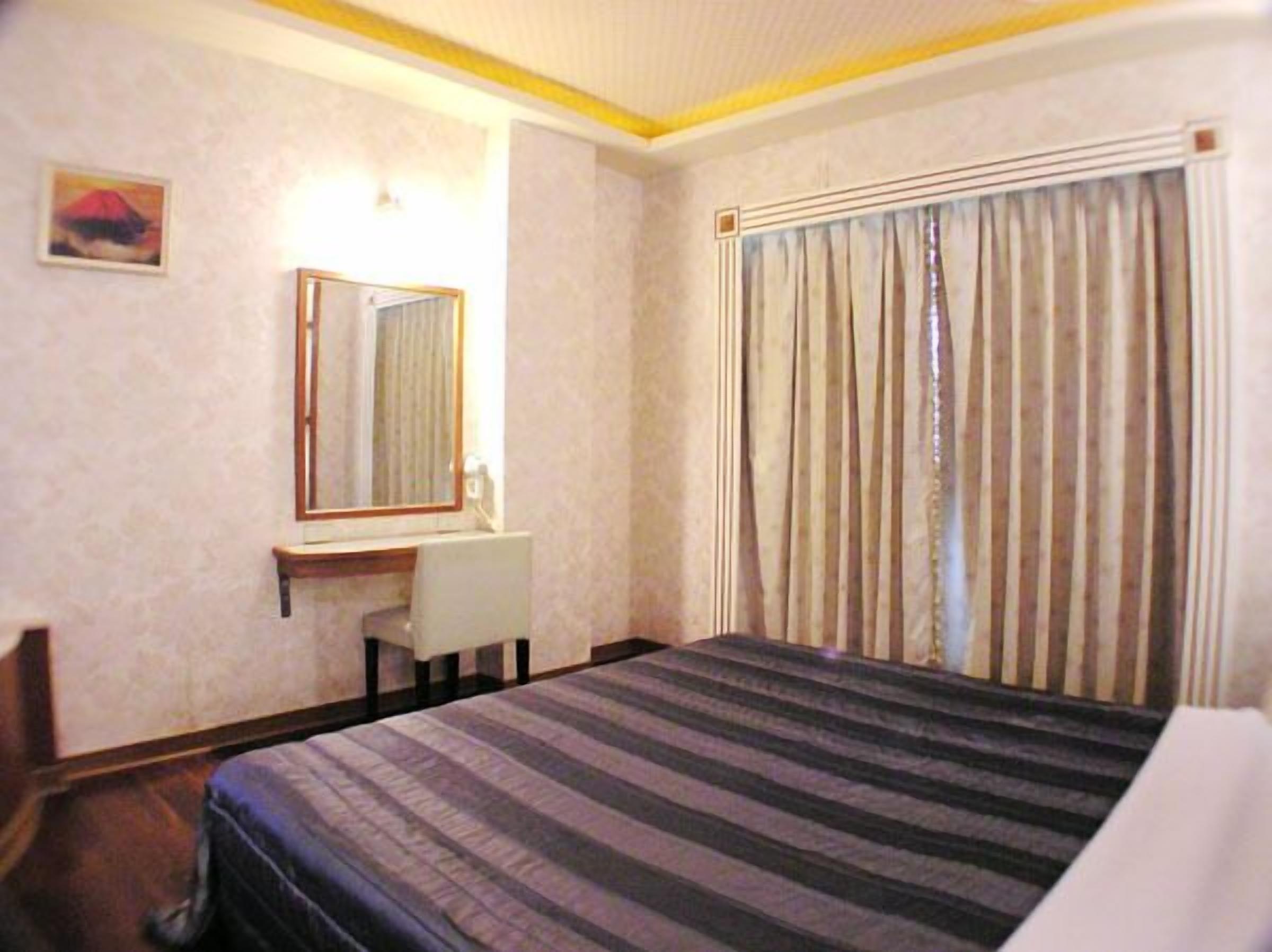 Habitación de hotel con cama, escritorio, silla, espejo y ventana con cortinas.