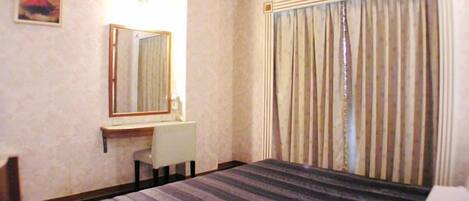 Habitación de hotel con cama, escritorio, silla, espejo y ventana con cortinas.