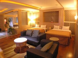 A hotel room with a bed, two sofas, a small round table, and a bathroom visible through an open door.