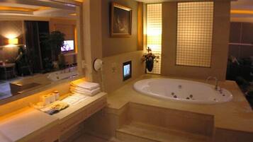 Un baño moderno con una bañera grande, un tocador con espejo y un televisor montado en la pared.