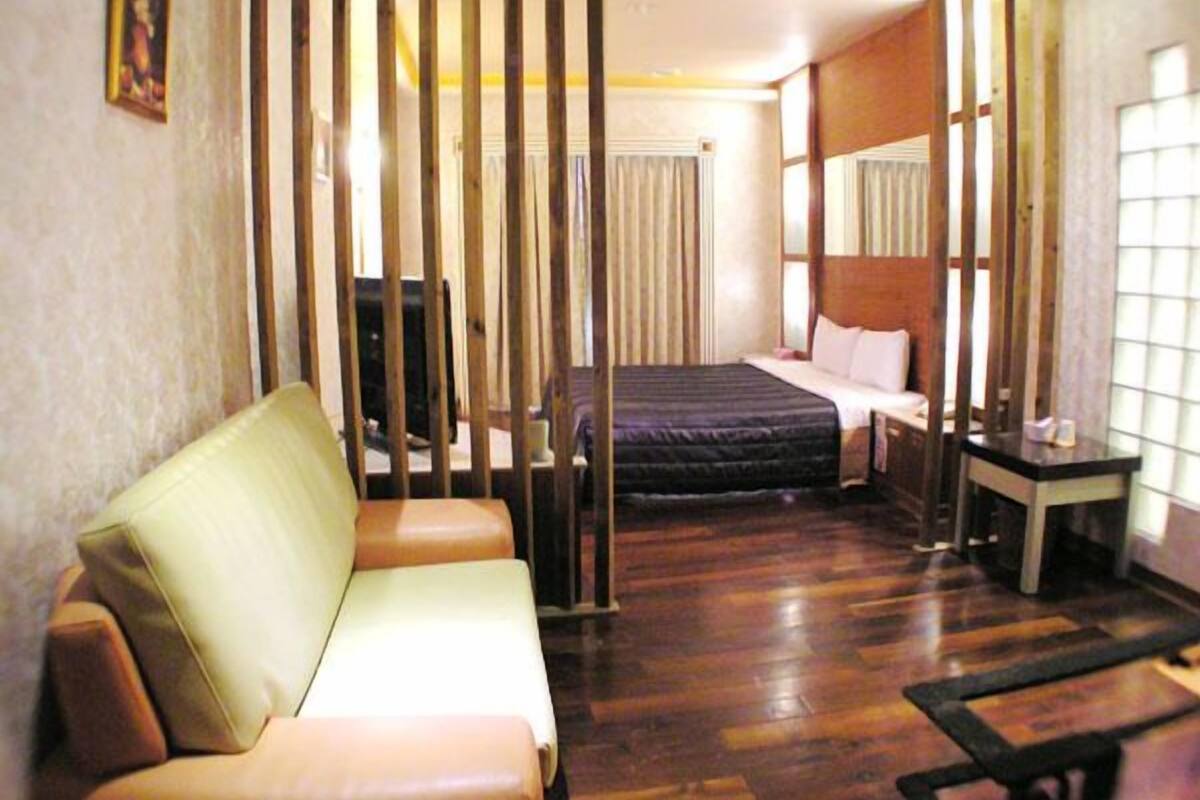 A hotel room with a wooden floor, a bed with white linens, a sofa, a small table, and a TV.