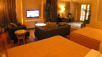 A hotel room with a bed, a sofa, a TV, a small table, and a chair.