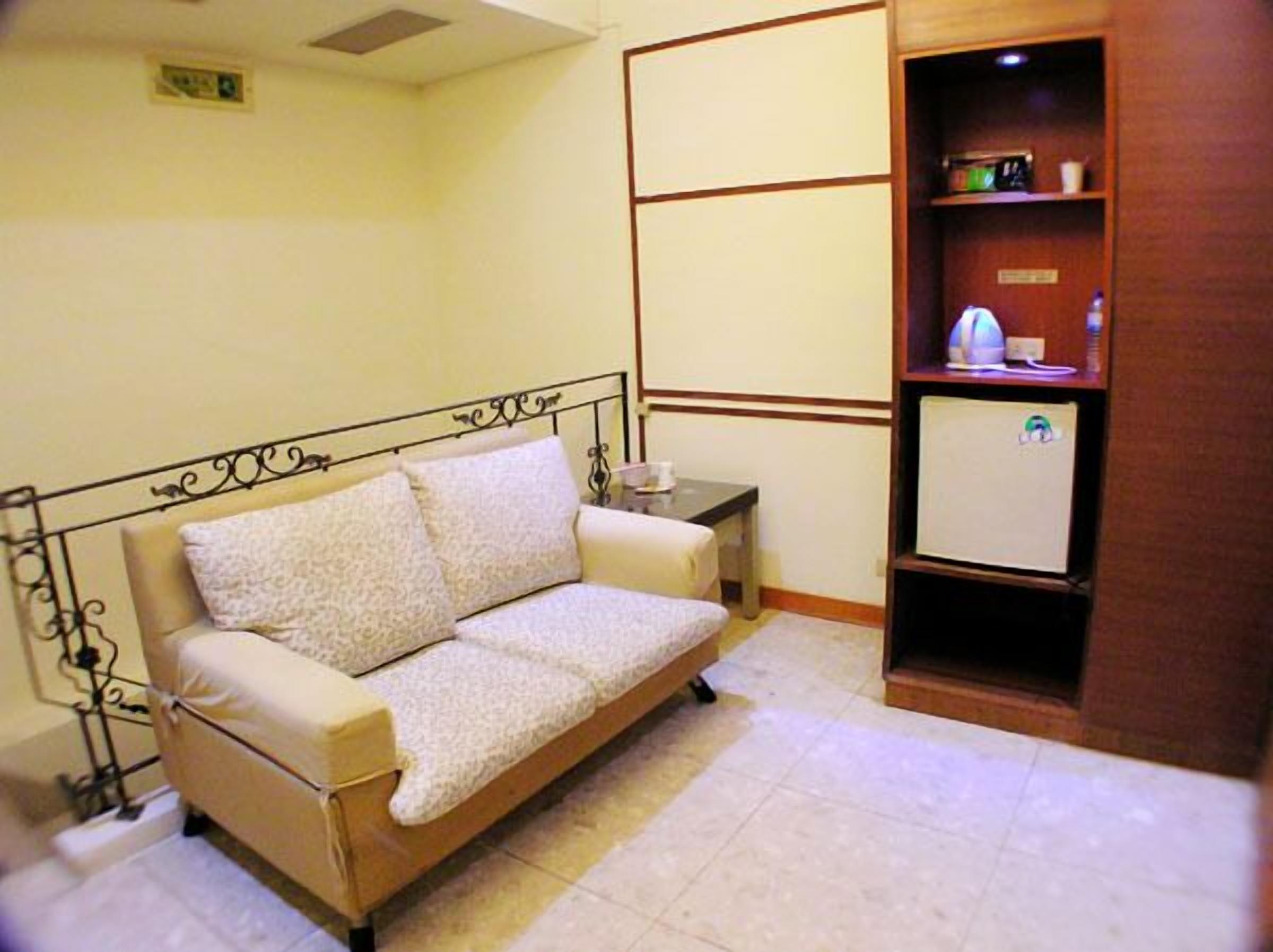 A small, single-room accommodation with a sofa bed, a bedside table, a small cabinet, and a wall-mounted shelf.