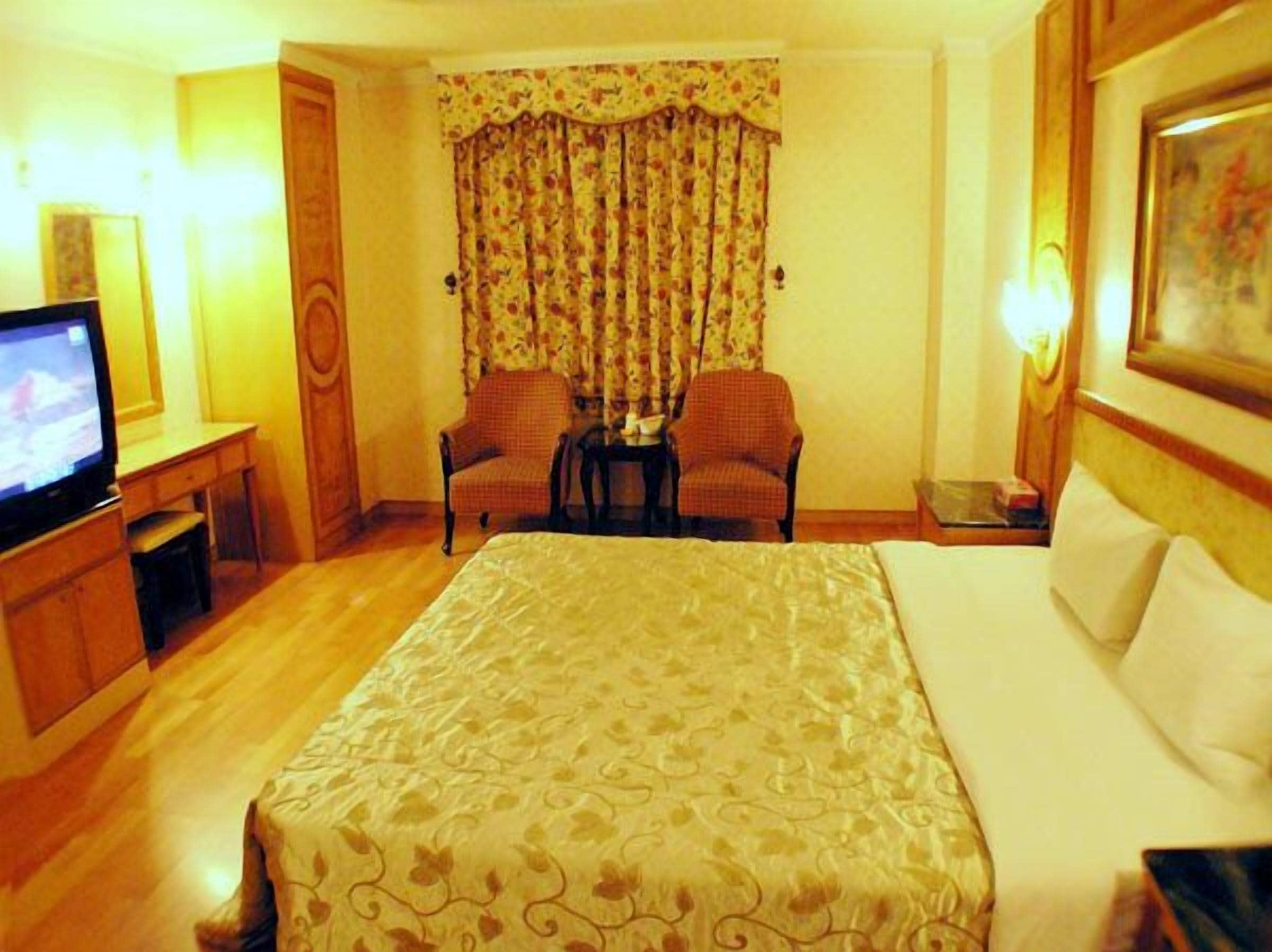 A hotel room with a bed, two armchairs, a television, and a painting on the wall.