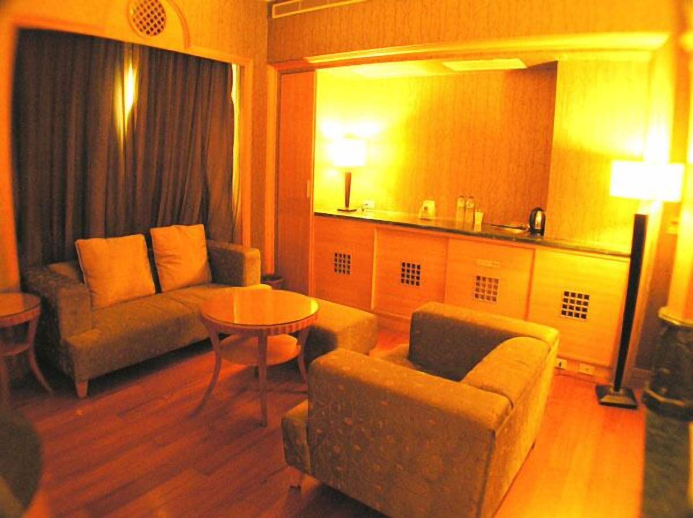 Ein Hotelzimmer mit einer Couch, einem Sessel und einem kleinen runden Tisch. Es gibt eine Küchenzeile mit einer Arbeitsplatte und Schränken.