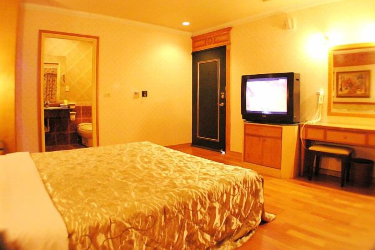 A hotel room with a bed, a television, a desk, and a door leading to a bathroom.