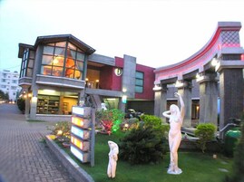 A modern building with a glass facade, outdoor sculptures, and a well-maintained garden.
