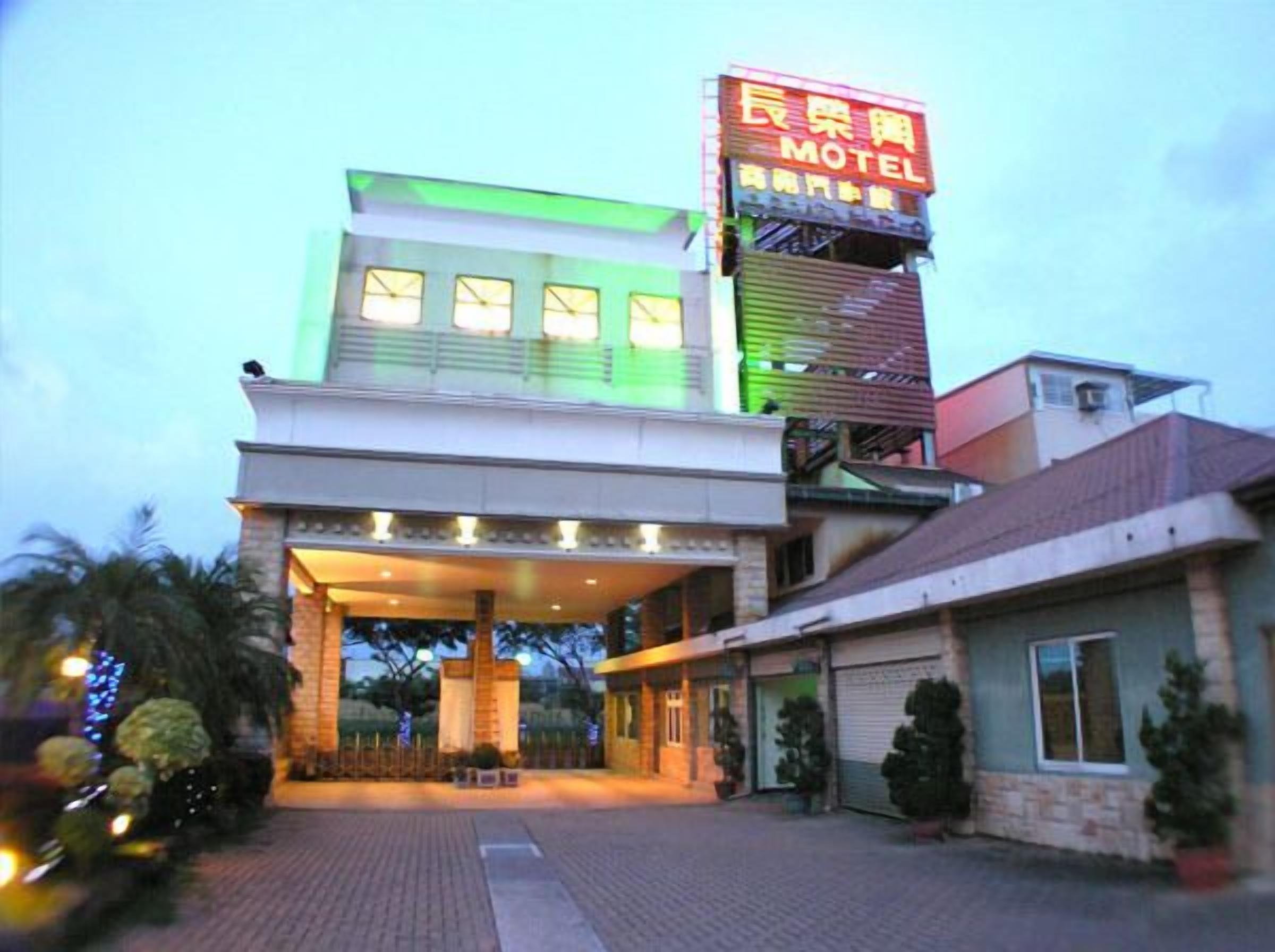 A motel with a prominent neon sign, a covered entrance, and a brick facade.