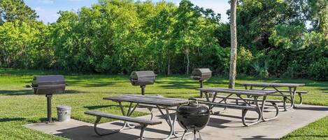 An outdoor picnic area with picnic tables, grills, and a trash can.
