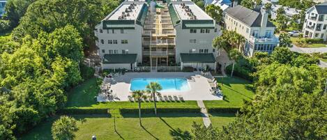 A large hotel with a central pool, surrounded by lush greenery and multiple buildings.