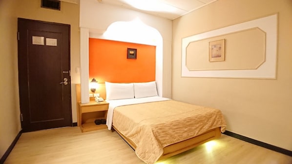 Una habitación de hotel con una cama, una mesita de noche, una lámpara, una puerta y un cuadro en la pared.