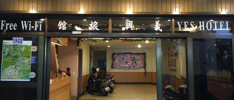 A hotel entrance with a sign for free Wi-Fi, a reception desk, and a motorcycle parked inside.