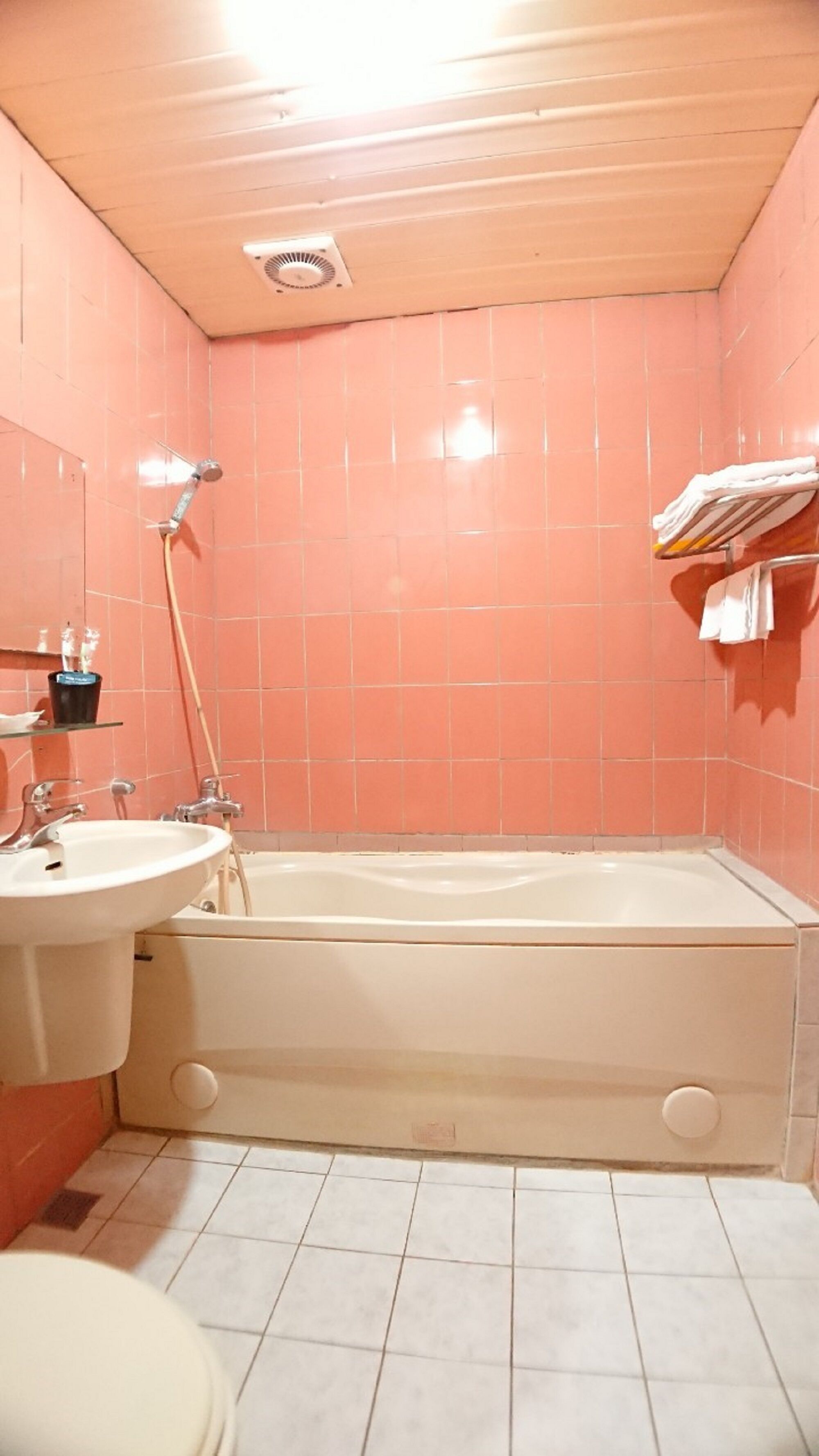 Un baño con azulejos rosas, un lavamanos blanco, una bañera y un inodoro.
