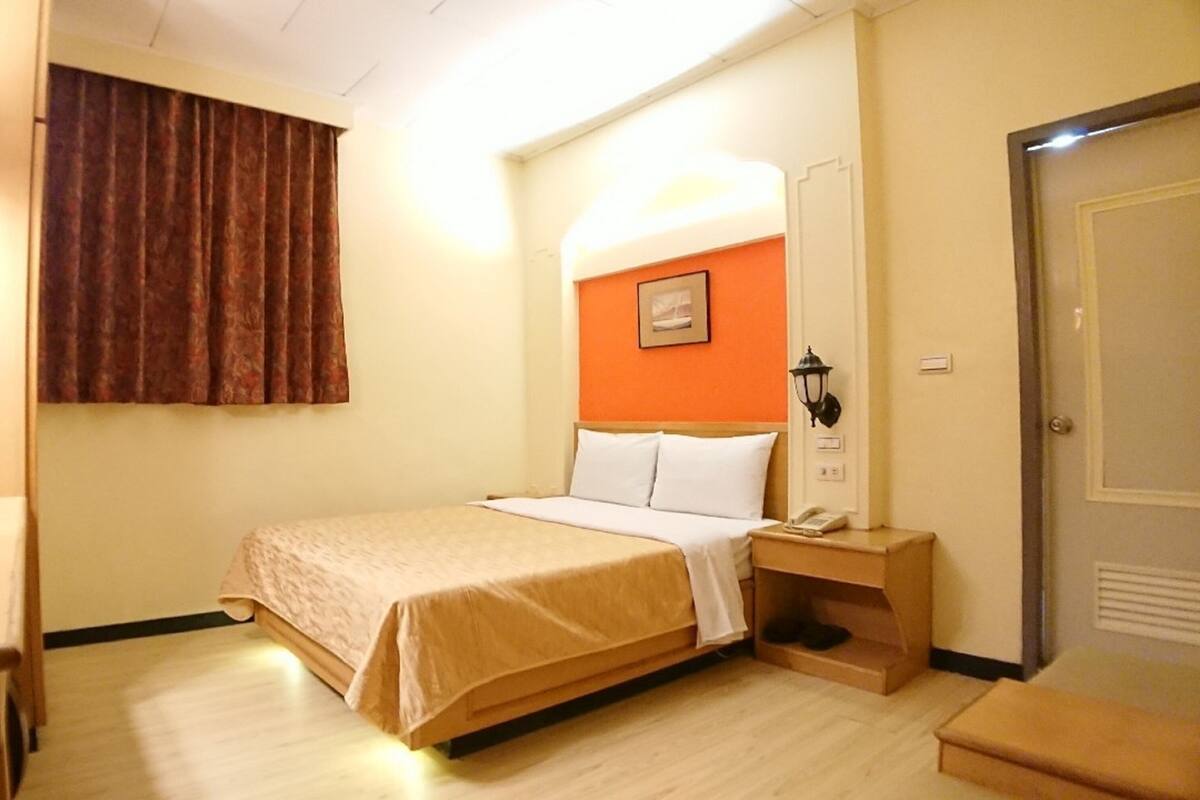 A hotel room with a bed, bedside table, lamp, and a door.