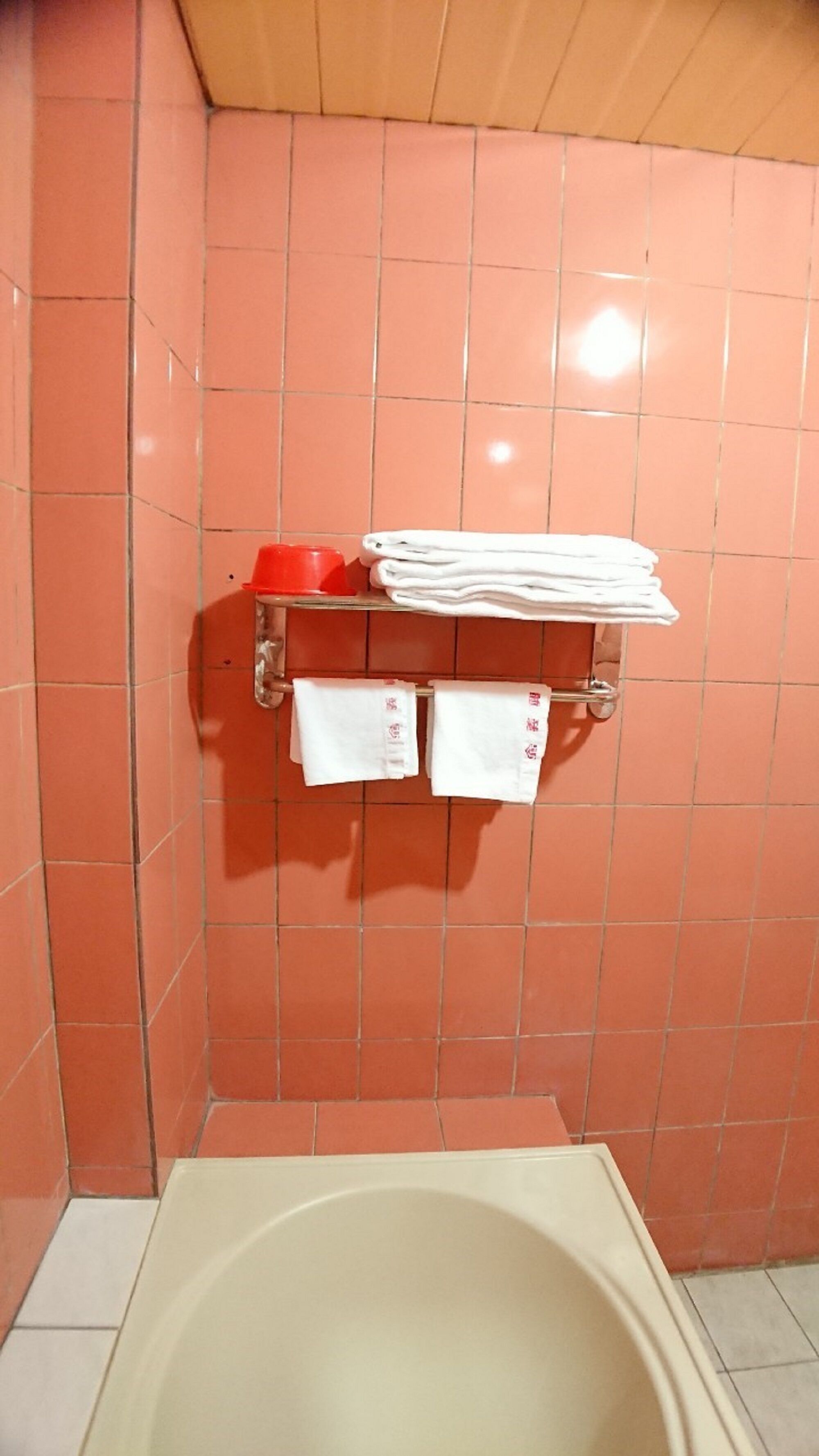 A bathroom with a bathtub, a towel rack with folded towels, and a red basin.