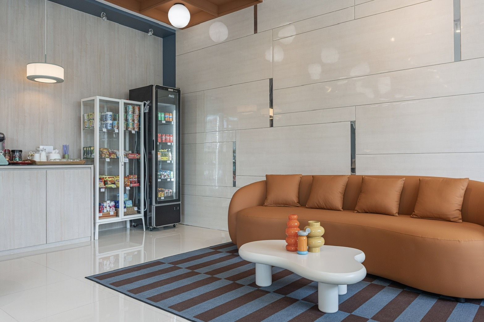 Una sala moderna con sofá, una mesita de centro con juguetes, un refrigerador lleno de bebidas y una cocina con refrigerador y alacena.