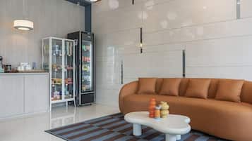 Una sala moderna con sofá, una mesita de centro con juguetes, un refrigerador lleno de bebidas y una cocina con refrigerador y alacena.