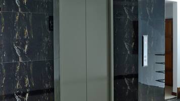 A modern elevator with a marble finish, a metallic door, and a control panel on the wall.