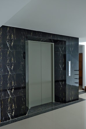 A modern elevator with a marble finish, a metallic door, and a control panel on the wall. - Charisma Residence (Rayong)